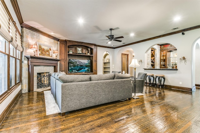 living room featuring ceiling fan, built in shelves, a fireplace, and crown molding