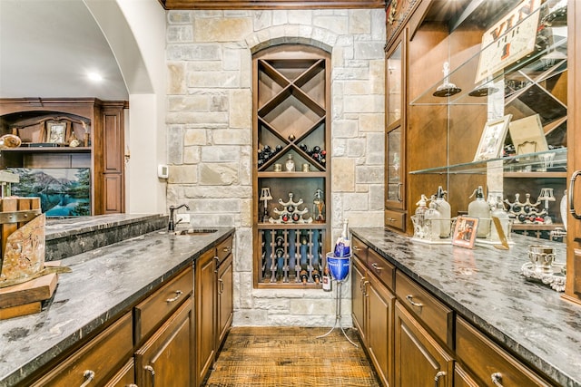 bar with dark hardwood / wood-style floors, dark stone counters, and sink