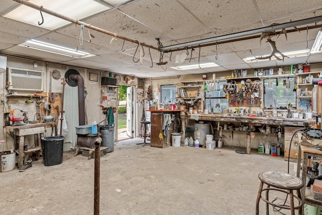 miscellaneous room with concrete flooring, a drop ceiling, an AC wall unit, and a workshop area