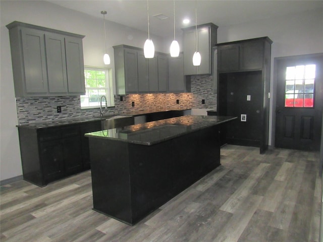 kitchen featuring hanging light fixtures, a center island, wood-type flooring, decorative backsplash, and dark stone counters