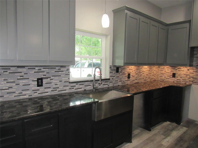 kitchen featuring sink, light hardwood / wood-style floors, decorative backsplash, decorative light fixtures, and dark stone counters