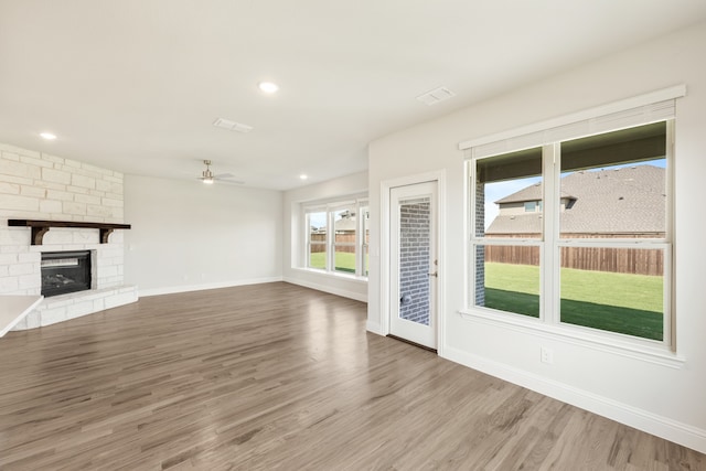 unfurnished living room with a stone fireplace, hardwood / wood-style floors, and ceiling fan