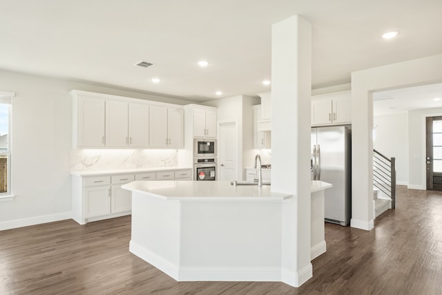 kitchen with decorative backsplash, appliances with stainless steel finishes, white cabinetry, a kitchen island with sink, and dark hardwood / wood-style floors