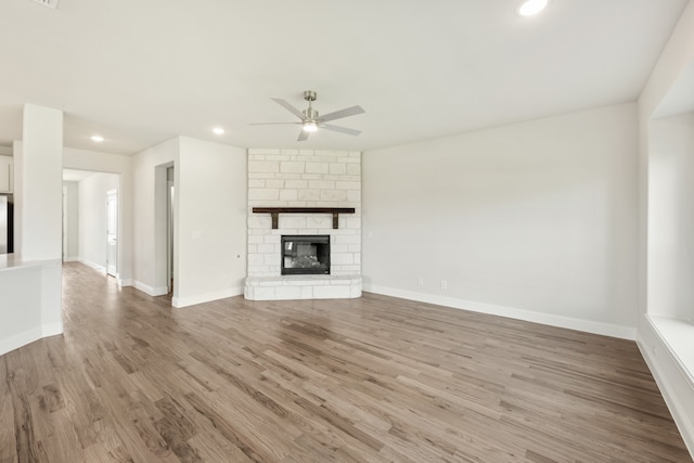 unfurnished living room with light hardwood / wood-style floors, a stone fireplace, and ceiling fan