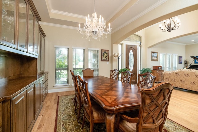 dining room with light wood-type flooring, a tray ceiling, arched walkways, and an inviting chandelier