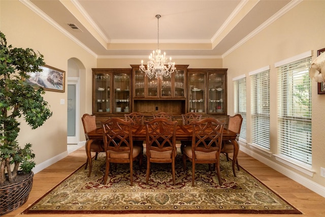 dining space with light wood finished floors, visible vents, a tray ceiling, and arched walkways