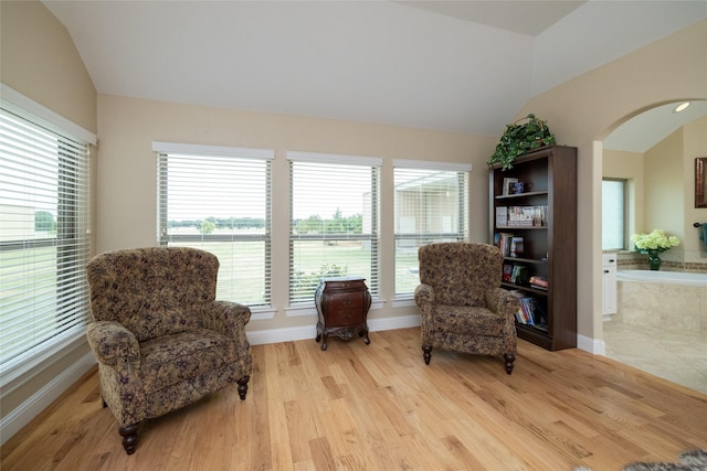 living area with light wood finished floors, baseboards, vaulted ceiling, and arched walkways