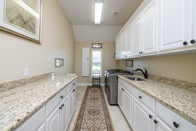 kitchen with visible vents, washing machine and dryer, white cabinets, a sink, and light tile patterned flooring