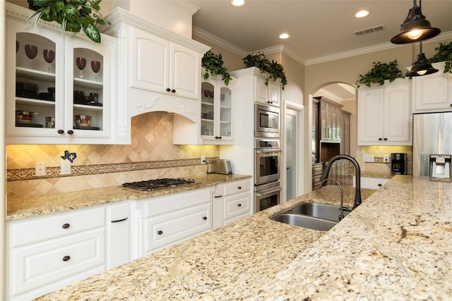 kitchen with glass insert cabinets, ornamental molding, light stone countertops, stainless steel appliances, and a sink