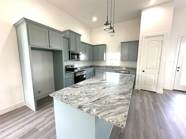 kitchen with stainless steel appliances, a center island, light stone counters, and hanging light fixtures