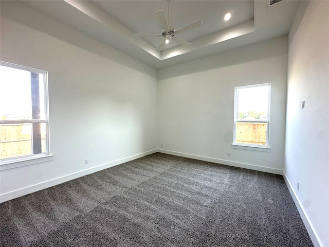 empty room with ceiling fan, dark colored carpet, and a tray ceiling