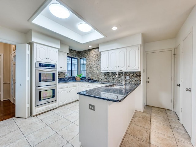 kitchen with stainless steel double oven, kitchen peninsula, white cabinets, and sink