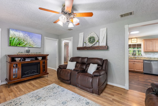 living room with ceiling fan, sink, a textured ceiling, and light hardwood / wood-style floors