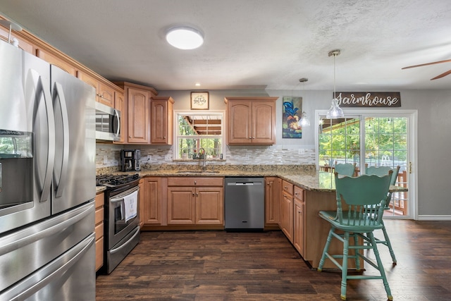 kitchen featuring sink, light stone counters, hanging light fixtures, dark hardwood / wood-style flooring, and stainless steel appliances