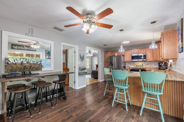 kitchen with dark hardwood / wood-style flooring, appliances with stainless steel finishes, a breakfast bar area, and light stone counters