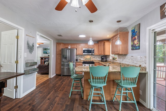 kitchen featuring a breakfast bar, appliances with stainless steel finishes, hanging light fixtures, dark hardwood / wood-style floors, and kitchen peninsula