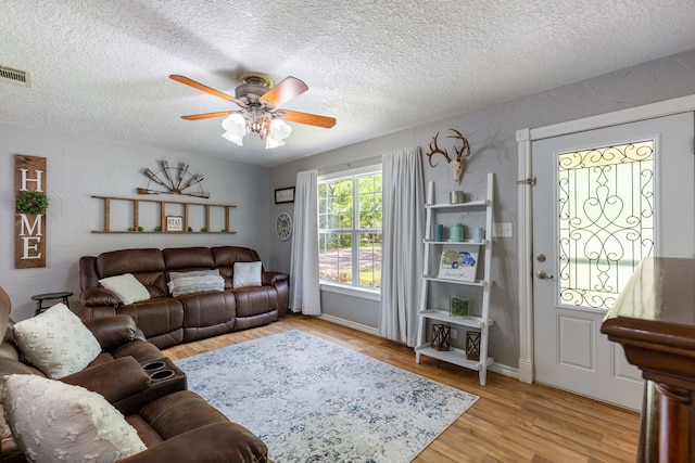 living room featuring a textured ceiling, ceiling fan, and light hardwood / wood-style flooring