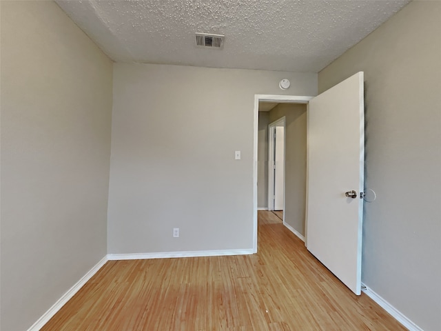 empty room with visible vents, a textured ceiling, baseboards, and wood finished floors