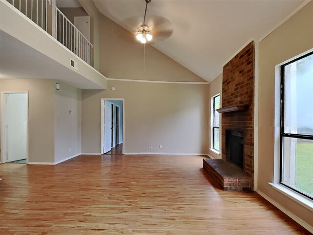 unfurnished living room featuring light hardwood / wood-style flooring, a brick fireplace, high vaulted ceiling, brick wall, and ceiling fan