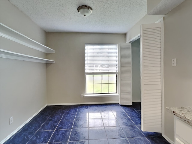 tiled empty room with a textured ceiling and baseboards