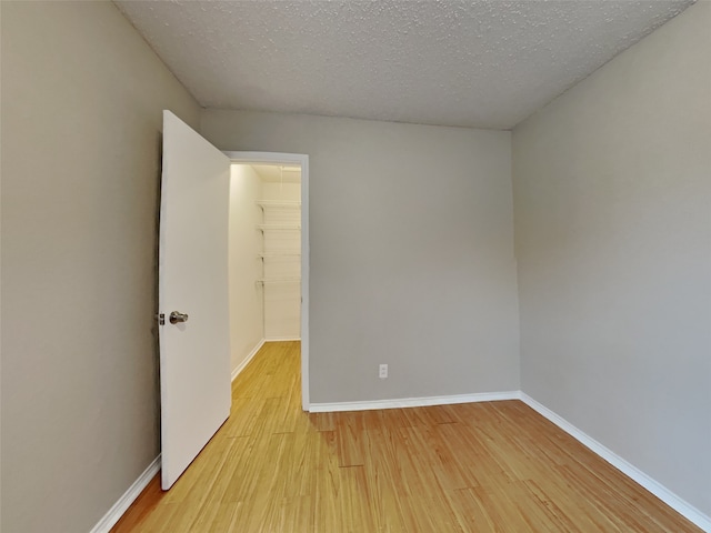 unfurnished room with a textured ceiling, light wood-style flooring, and baseboards