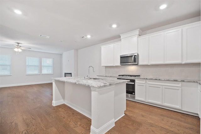 kitchen featuring appliances with stainless steel finishes, ceiling fan, a center island with sink, hardwood / wood-style flooring, and white cabinets