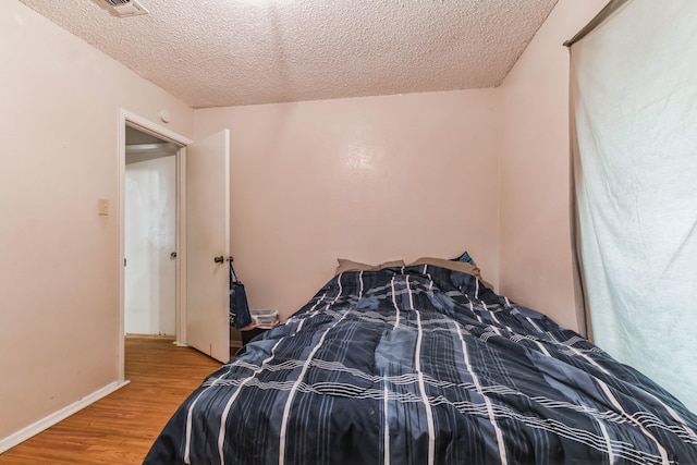 bedroom with visible vents, a textured ceiling, baseboards, and wood finished floors