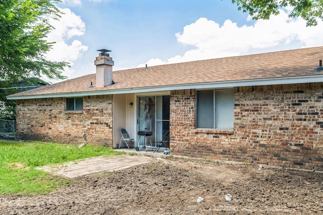 back of house featuring brick siding, a chimney, and roof with shingles