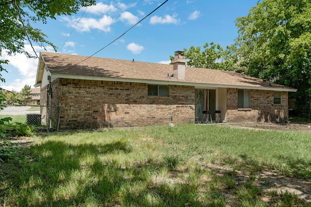 back of property with brick siding, a chimney, a shingled roof, and fence