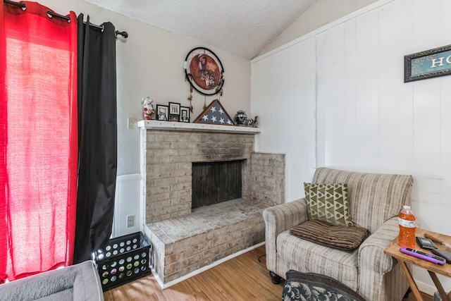 living area featuring a fireplace, a textured ceiling, lofted ceiling, and hardwood / wood-style floors