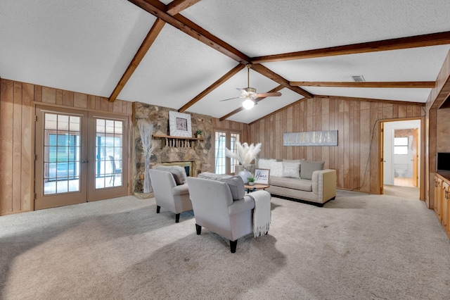 living area featuring light carpet, vaulted ceiling with beams, wood walls, and a stone fireplace