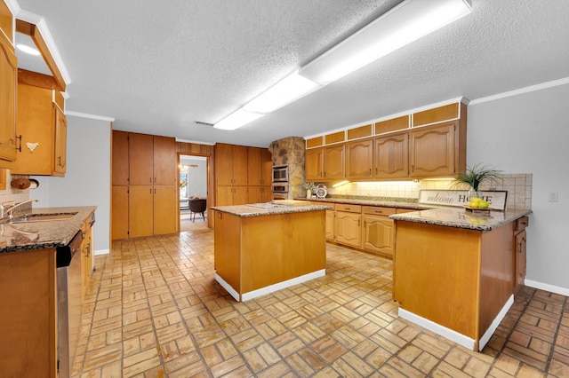 kitchen featuring a sink, backsplash, a center island, brown cabinetry, and dark stone countertops