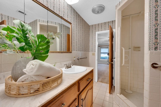 full bath with a wainscoted wall, visible vents, vanity, tiled shower, and wallpapered walls