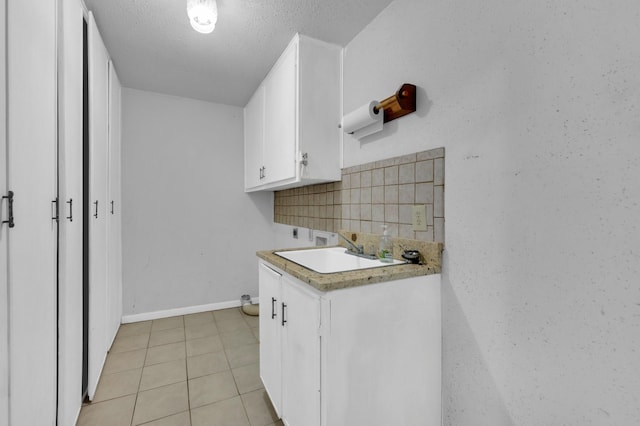 kitchen featuring light tile patterned flooring, a sink, baseboards, white cabinets, and light countertops