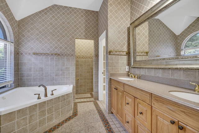 bathroom featuring a relaxing tiled tub, vaulted ceiling, double vanity, tile walls, and tile patterned flooring