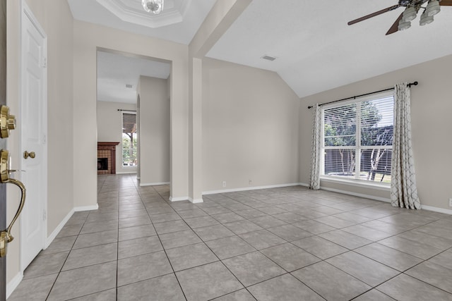 empty room featuring crown molding, light tile patterned floors, ceiling fan, a brick fireplace, and a raised ceiling