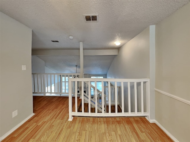 hall featuring hardwood / wood-style flooring, vaulted ceiling, and a textured ceiling