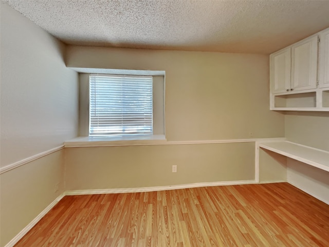 interior space featuring light hardwood / wood-style floors, a textured ceiling, and built in desk