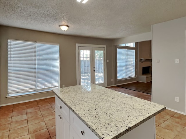 kitchen with white cabinetry, french doors, light tile patterned floors, a center island, and light stone counters