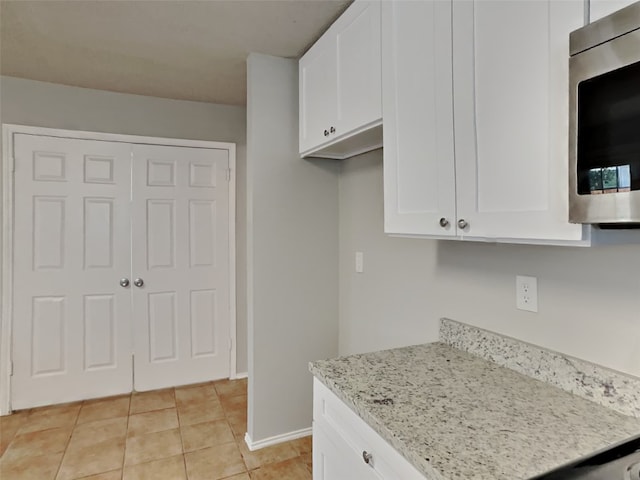 kitchen with light tile patterned flooring, white cabinetry, and light stone countertops