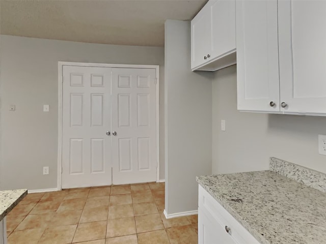 kitchen with white cabinetry, light tile patterned floors, and light stone counters