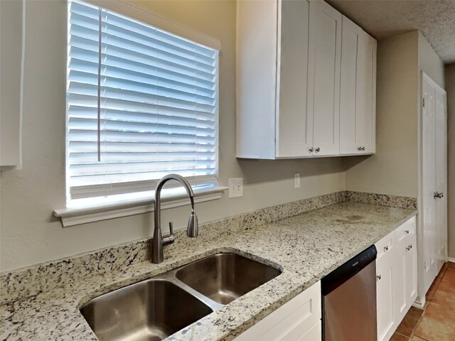 kitchen with white cabinets, sink, light tile patterned floors, light stone countertops, and dishwasher