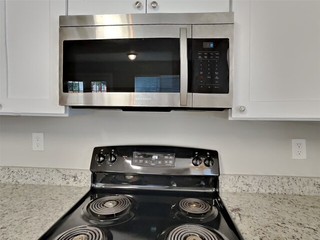 room details featuring black electric range oven, white cabinetry, and light stone counters