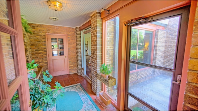 interior space with brick wall, tile patterned flooring, and ornamental molding