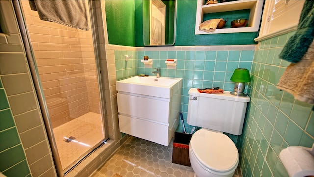 bathroom with a shower with door, toilet, vanity, tile walls, and tile patterned floors