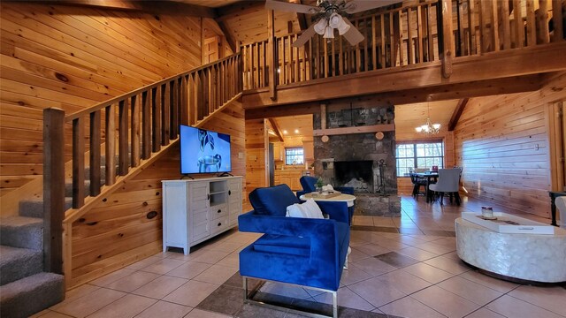 living room with beamed ceiling, tile patterned flooring, stairs, wood walls, and ceiling fan with notable chandelier