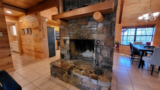 living room featuring wooden walls, wooden ceiling, a stone fireplace, a chandelier, and beam ceiling