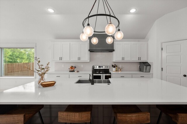 kitchen with a kitchen bar, stainless steel electric range, lofted ceiling, and a center island with sink