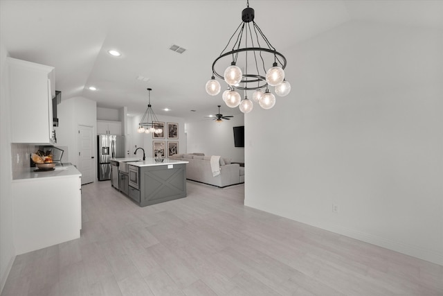 kitchen featuring white cabinetry, ceiling fan with notable chandelier, an island with sink, appliances with stainless steel finishes, and decorative light fixtures