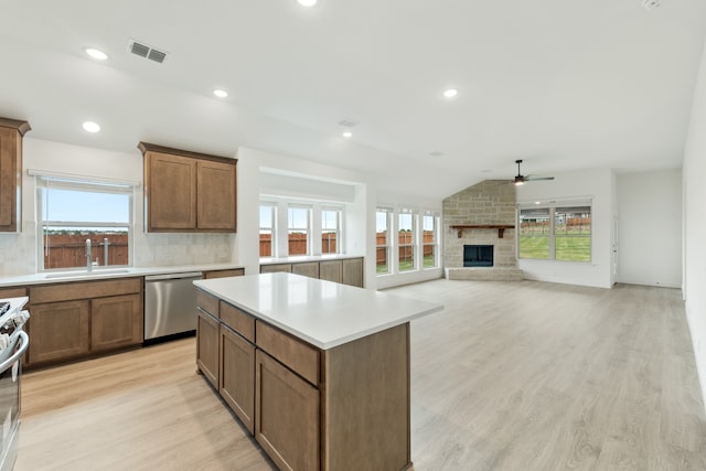 kitchen featuring light hardwood / wood-style floors, a stone fireplace, stainless steel appliances, lofted ceiling, and sink